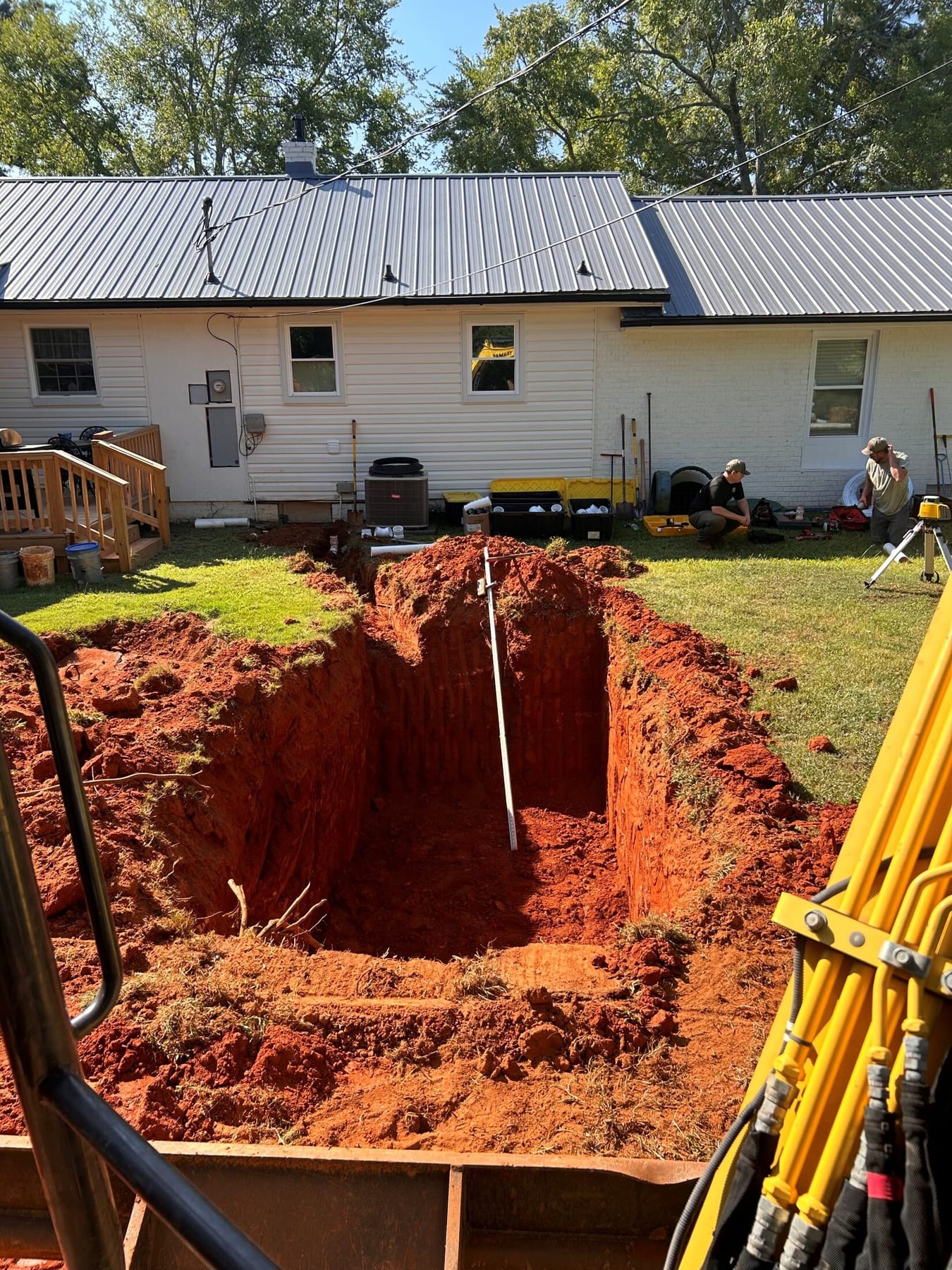 An open septic excavation behind a house in Upstate South Carolina, cut into red clay.
