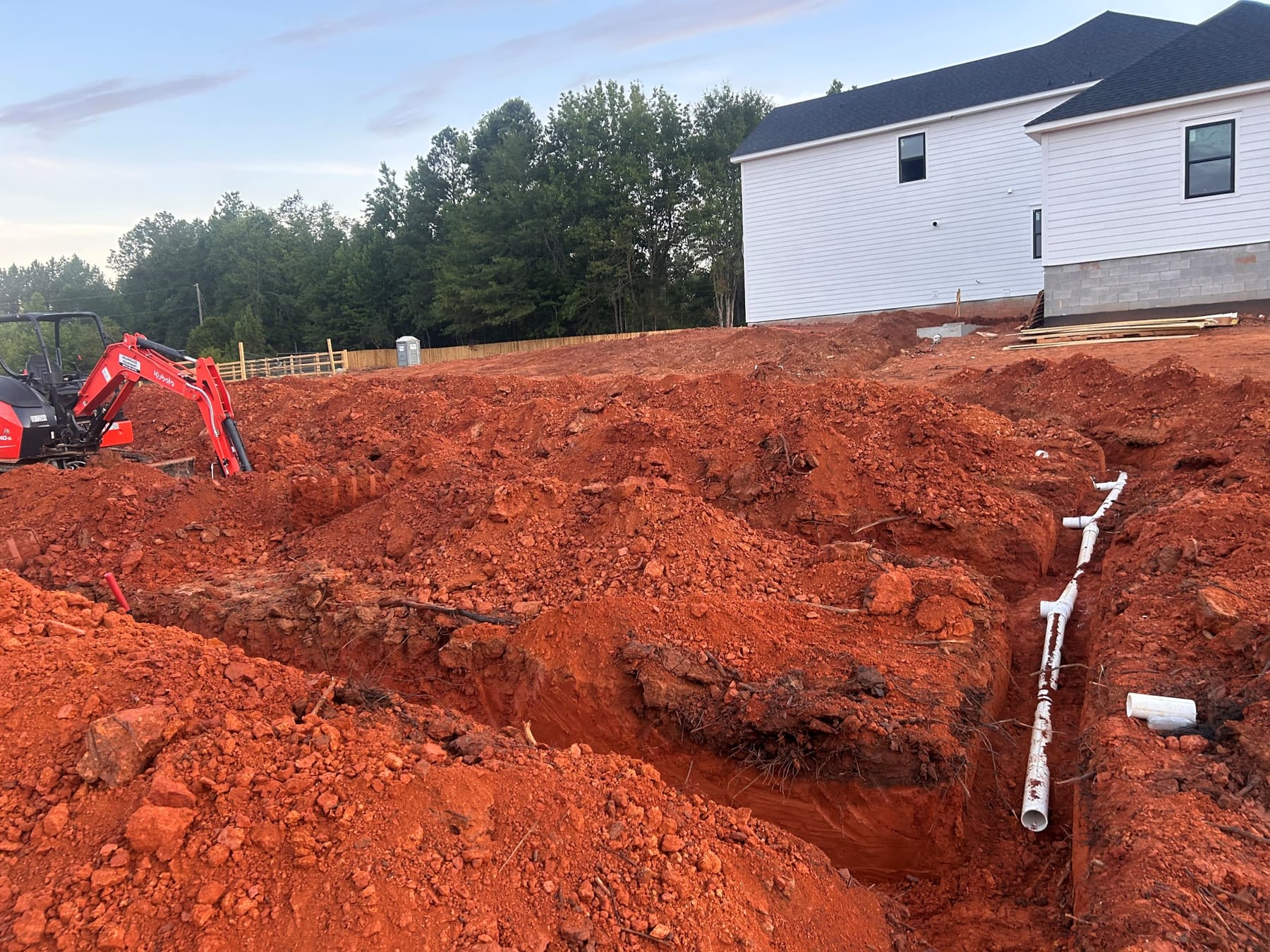 An excavator opening a cut for a new septic system at a rural building site.