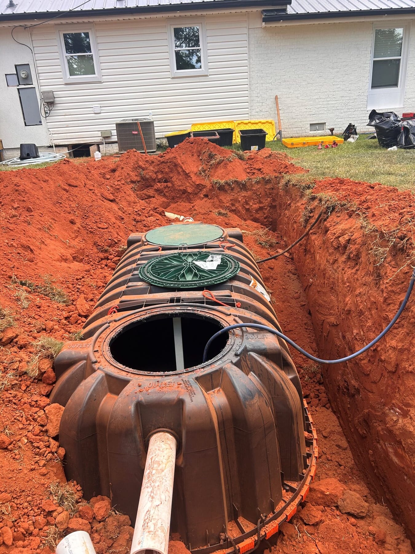 A new septic tank set into an excavation beside a house, riser visible at grade.