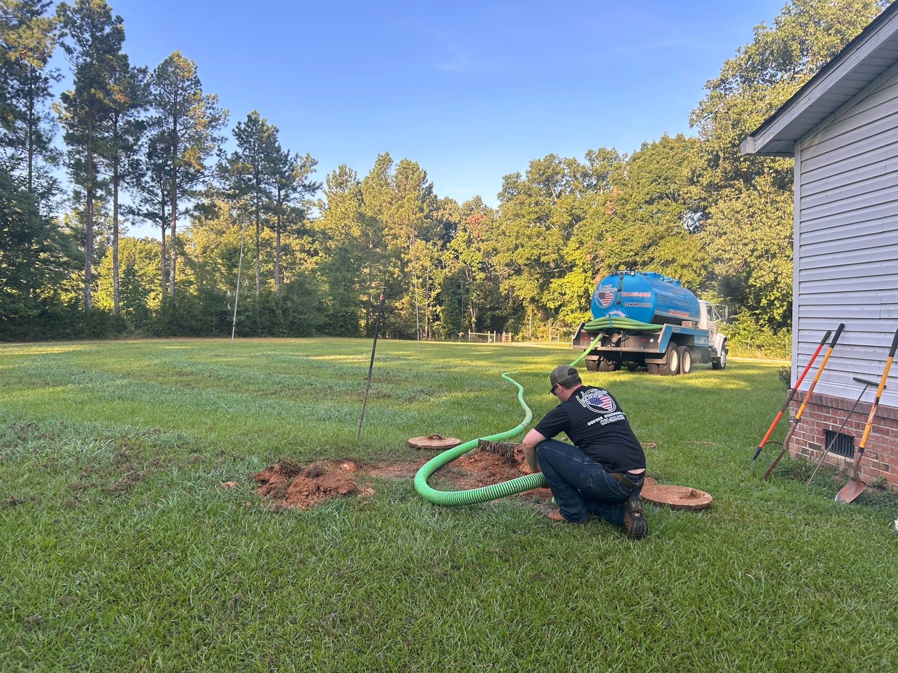A technician working at an uncovered septic tank with the suction hose run out across the lawn.
